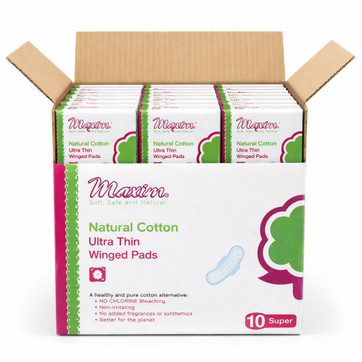 Open cardboard case holding multiple packs of Maxim Natural Cotton Ultra Thin Winged Pads. The front panel shows the Maxim logo and product name, a small pad icon, and benefit bullets (‘no chlorine bleaching,’ ‘non-irritating,’ ‘no added fragrances or syn